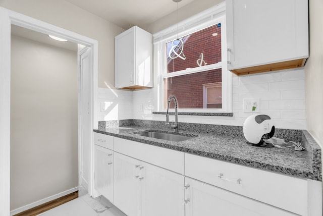 kitchen with a sink, dark stone countertops, white cabinetry, decorative backsplash, and baseboards