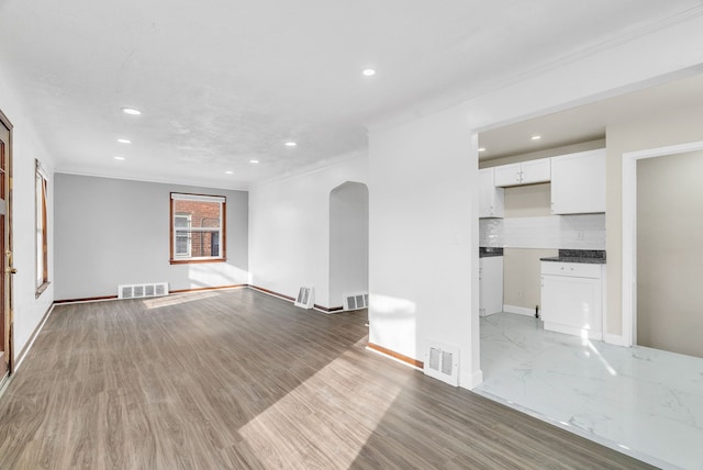 unfurnished living room featuring arched walkways, visible vents, and ornamental molding