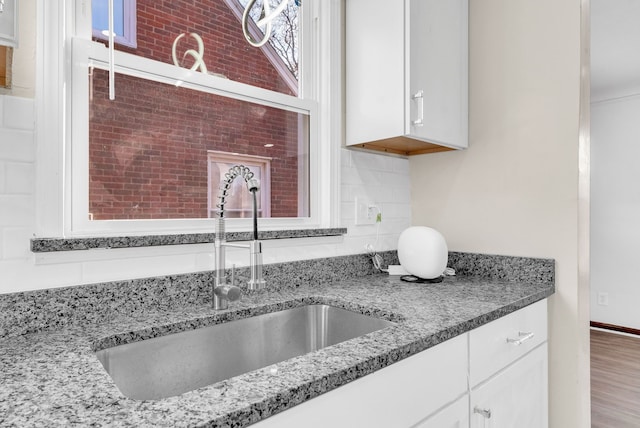 kitchen featuring tasteful backsplash, white cabinetry, light stone counters, and a sink