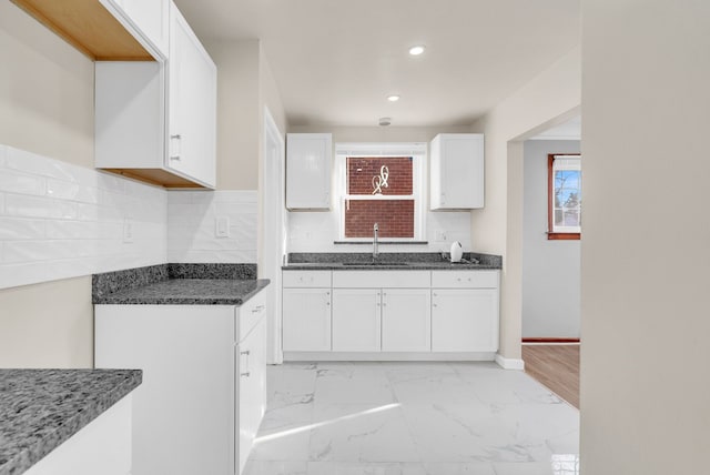 kitchen with backsplash, marble finish floor, white cabinetry, and a sink