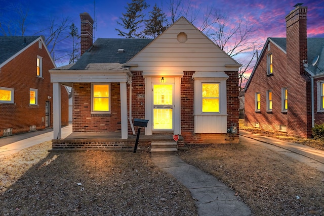 bungalow-style home with a porch, brick siding, and a chimney