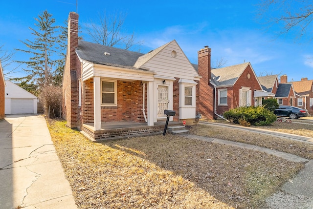 bungalow-style house with brick siding, a chimney, a detached garage, and an outdoor structure