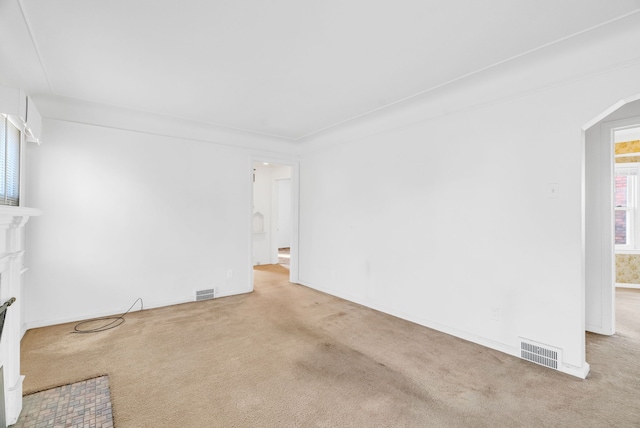 carpeted empty room with visible vents, arched walkways, and a fireplace