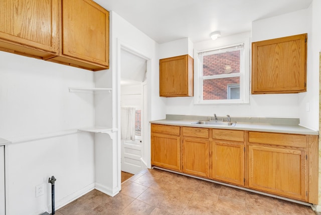 kitchen with a sink, baseboards, light countertops, brown cabinetry, and open shelves