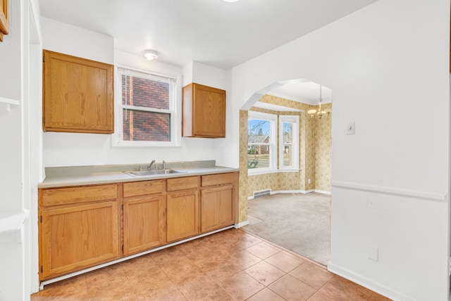 kitchen featuring baseboards, visible vents, arched walkways, a sink, and light countertops