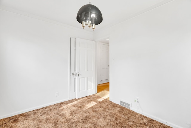 carpeted spare room with visible vents, baseboards, a notable chandelier, and ornamental molding