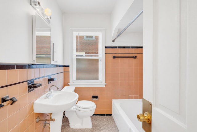 bathroom featuring toilet, a tub to relax in, tile walls, wainscoting, and tile patterned flooring