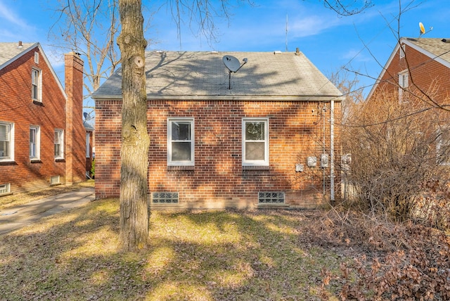 back of house featuring brick siding, roof with shingles, and a lawn