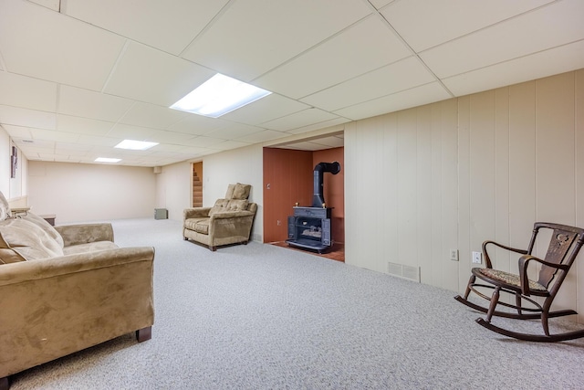 carpeted living area with a wood stove, a paneled ceiling, and visible vents