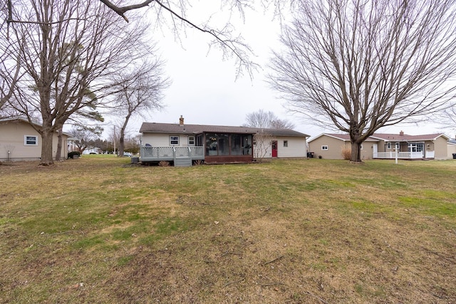 rear view of property featuring a lawn, a chimney, and a sunroom