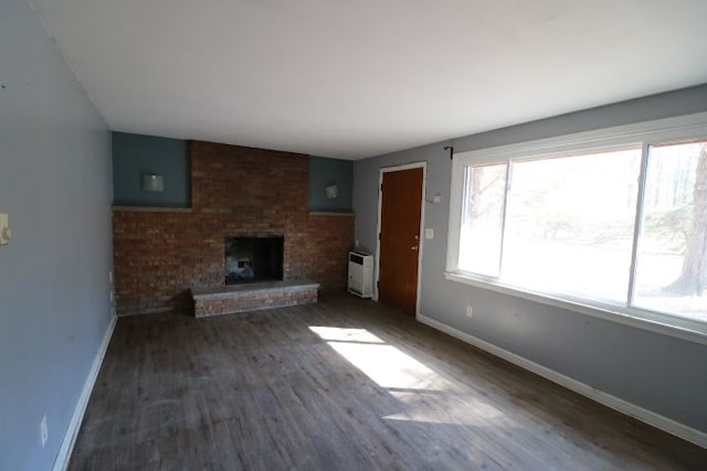 unfurnished living room featuring wood finished floors, heating unit, a fireplace, and baseboards