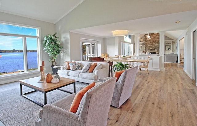 living area with light wood finished floors, crown molding, a water view, vaulted ceiling, and ornate columns