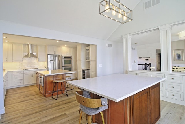 kitchen featuring visible vents, a kitchen island, decorative columns, stainless steel appliances, and wall chimney range hood