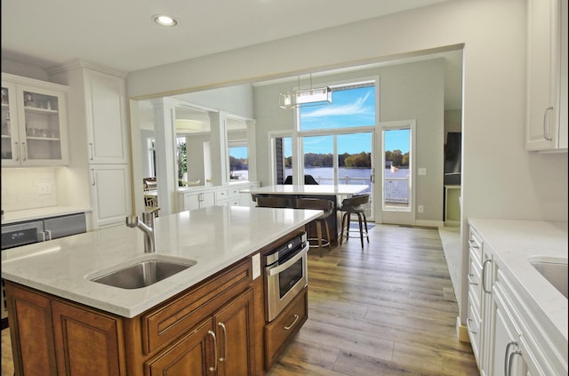 kitchen with light wood-style flooring, a kitchen island with sink, a sink, decorative backsplash, and ornate columns