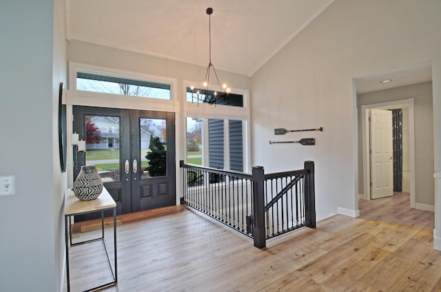 entrance foyer with baseboards, high vaulted ceiling, an inviting chandelier, light wood-style floors, and crown molding