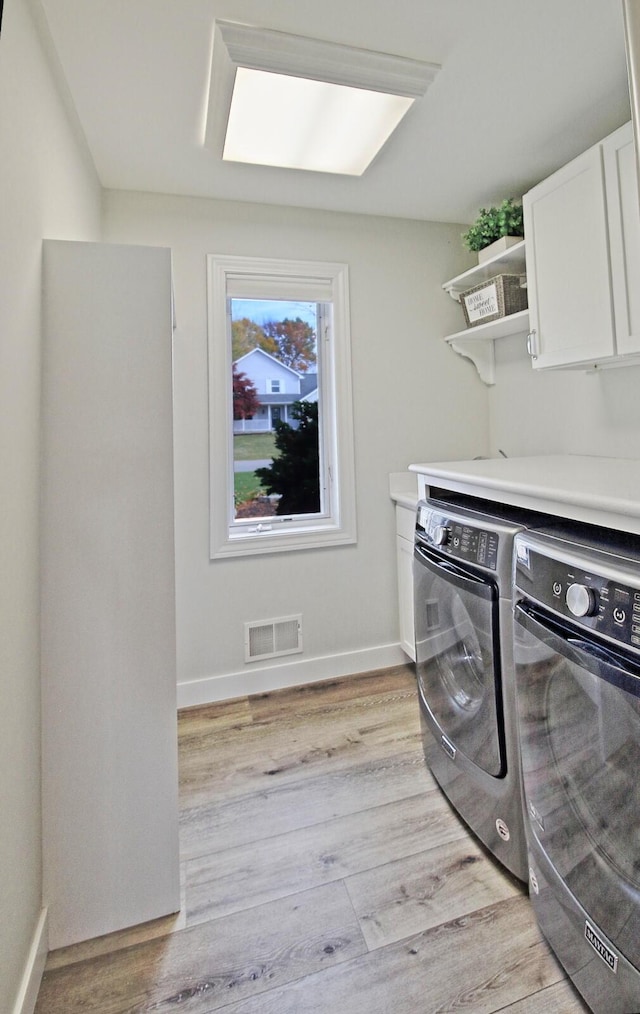 washroom featuring visible vents, cabinet space, washer and dryer, and light wood-style flooring