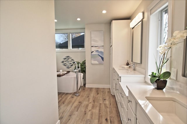 full bath with a wealth of natural light, a soaking tub, vanity, and wood finished floors