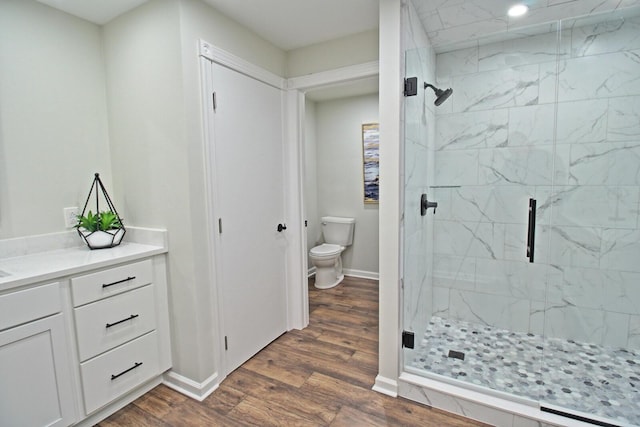 bathroom with a marble finish shower, baseboards, toilet, and wood finished floors