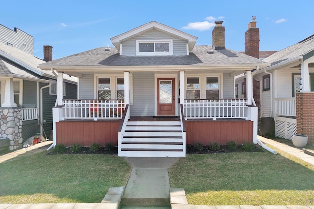 bungalow-style home featuring a front lawn, a chimney, covered porch, and a shingled roof