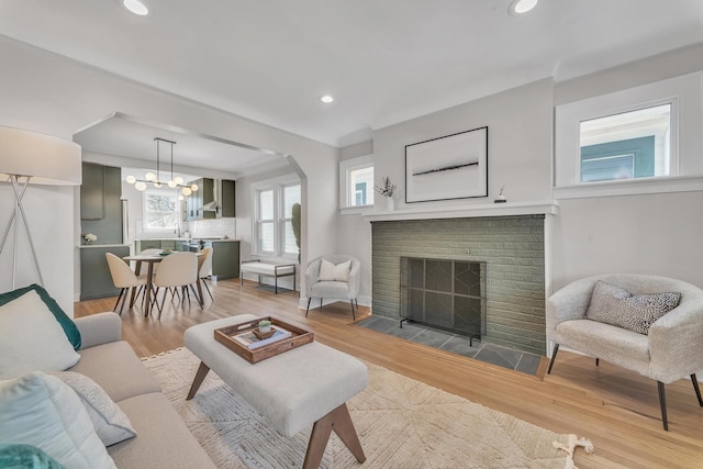 living room featuring light wood-type flooring, recessed lighting, arched walkways, an inviting chandelier, and a brick fireplace