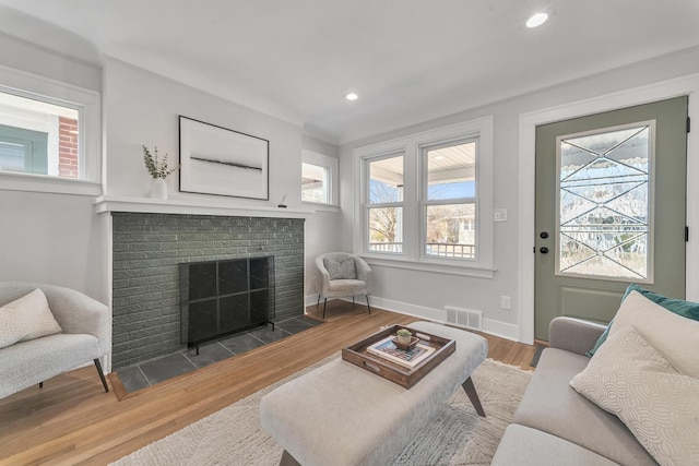 living area featuring wood finished floors, visible vents, baseboards, recessed lighting, and a brick fireplace