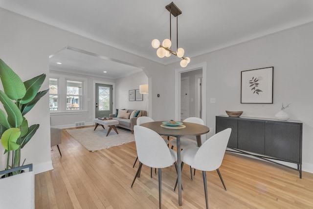 dining space with visible vents, light wood-style flooring, arched walkways, baseboards, and a chandelier