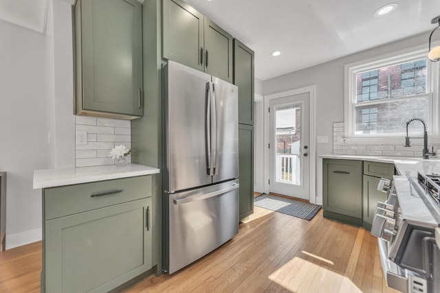 kitchen featuring green cabinetry, light countertops, light wood-style floors, stainless steel appliances, and a sink