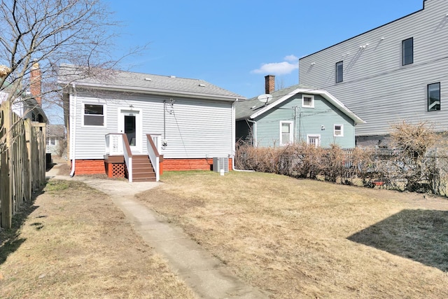 back of property featuring a lawn, central AC, roof with shingles, and fence