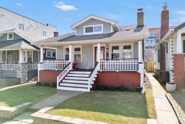 bungalow-style home with covered porch, a chimney, and a front lawn