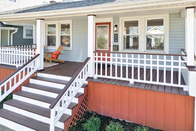 view of exterior entry with covered porch and a shingled roof