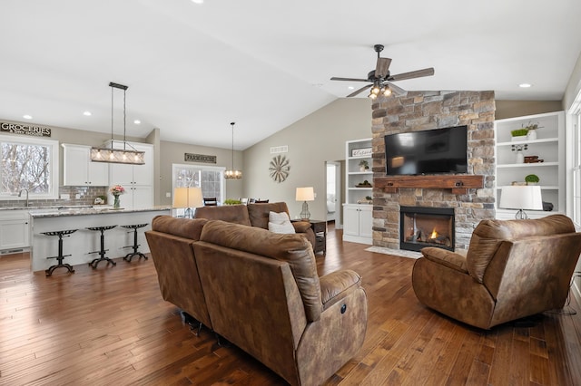 living room with dark wood finished floors, lofted ceiling, recessed lighting, ceiling fan, and a stone fireplace