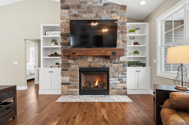 living room featuring baseboards, wood-type flooring, a stone fireplace, and vaulted ceiling