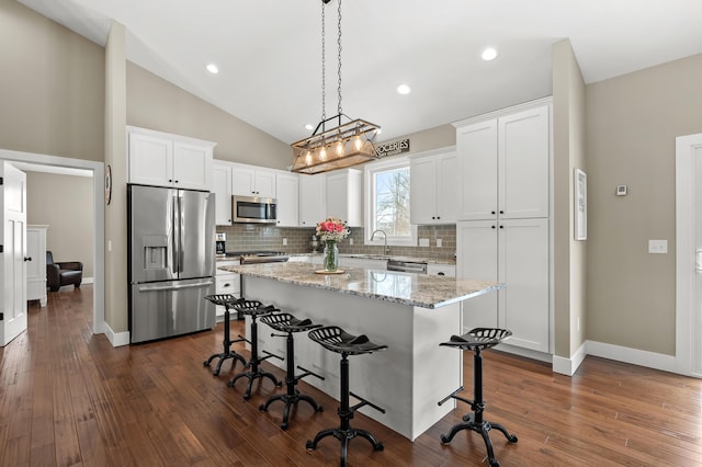 kitchen featuring a kitchen island, a breakfast bar, vaulted ceiling, appliances with stainless steel finishes, and white cabinetry