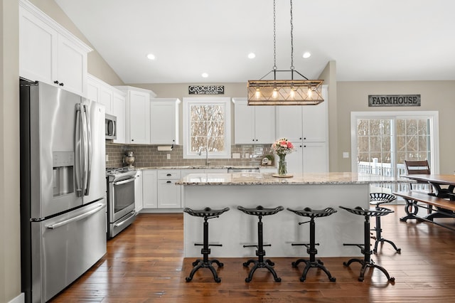 kitchen featuring a breakfast bar, lofted ceiling, stainless steel appliances, white cabinetry, and a sink