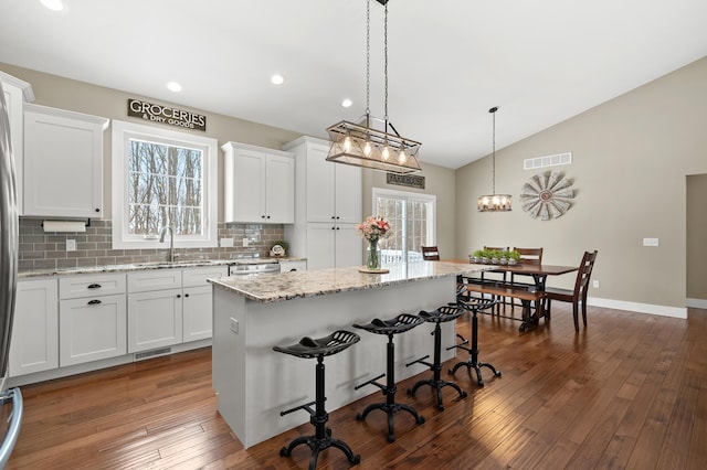 kitchen featuring visible vents, lofted ceiling, a kitchen island, and white cabinetry