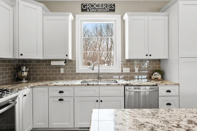 kitchen featuring a wealth of natural light, a sink, backsplash, white cabinetry, and stainless steel appliances