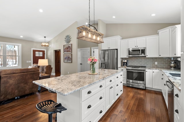 kitchen with dark wood finished floors, open floor plan, appliances with stainless steel finishes, a breakfast bar area, and lofted ceiling