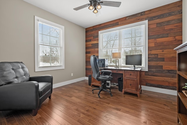 office area featuring wooden walls, a ceiling fan, baseboards, and wood finished floors