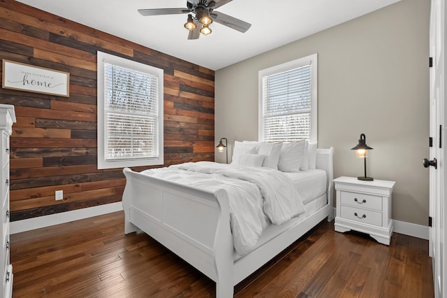 bedroom with dark wood finished floors, wooden walls, a ceiling fan, and baseboards