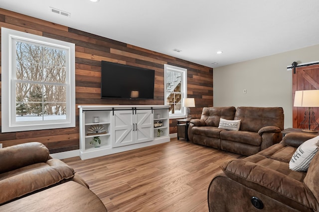 living area featuring a barn door, wooden walls, visible vents, and light wood finished floors