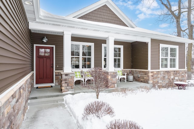 snow covered property entrance featuring stone siding and a porch