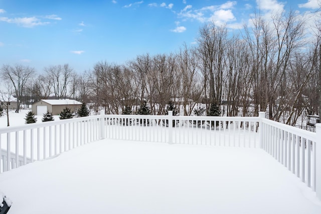 snowy yard featuring an outbuilding, a garage, and a wooden deck