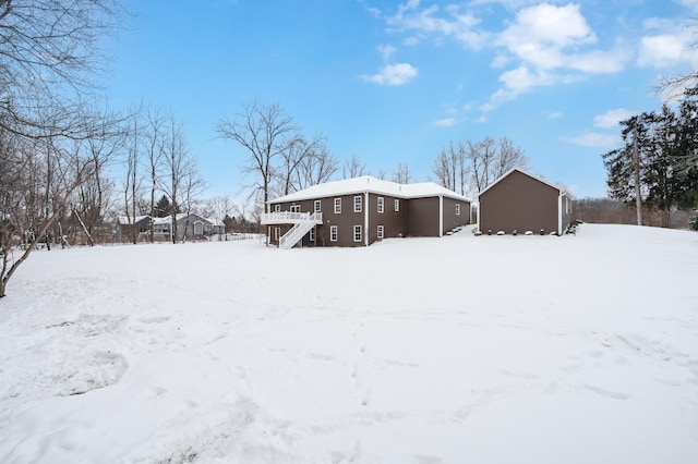 snow covered back of property featuring a storage unit, a deck, an outdoor structure, and stairway