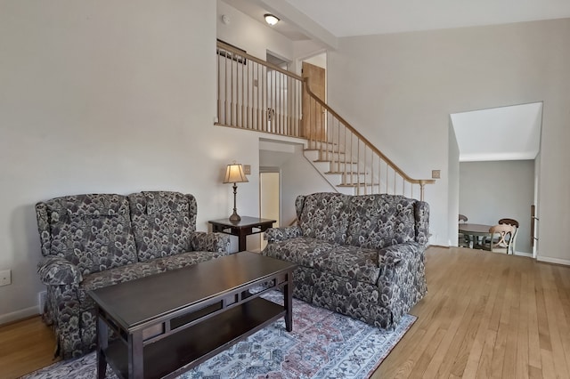 living area with stairway, baseboards, a towering ceiling, and hardwood / wood-style flooring