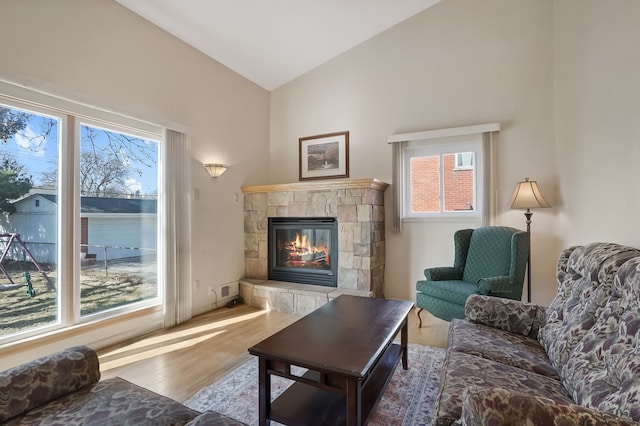 living room with a wealth of natural light, lofted ceiling, wood finished floors, and a tiled fireplace