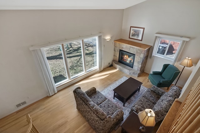 living area with a stone fireplace, vaulted ceiling, visible vents, and light wood finished floors