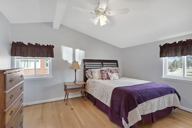 bedroom with multiple windows, baseboards, lofted ceiling with beams, and light wood-style floors