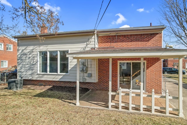 rear view of house featuring a yard, brick siding, central AC, and a chimney