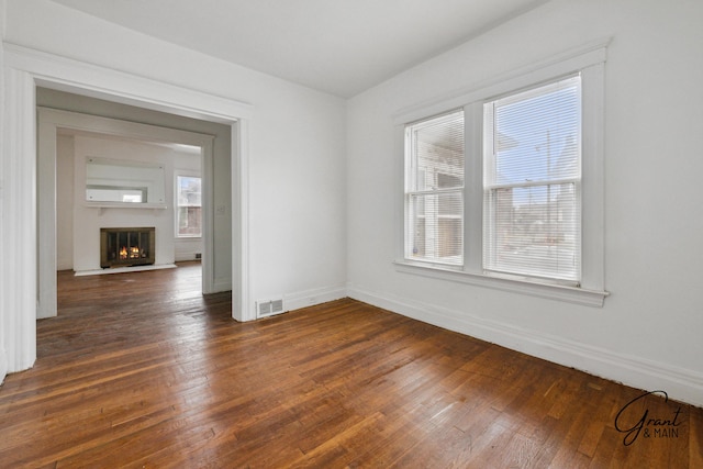 unfurnished room featuring dark wood finished floors, baseboards, visible vents, and a lit fireplace