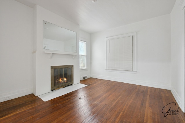 unfurnished living room featuring a fireplace with flush hearth, baseboards, visible vents, and hardwood / wood-style flooring